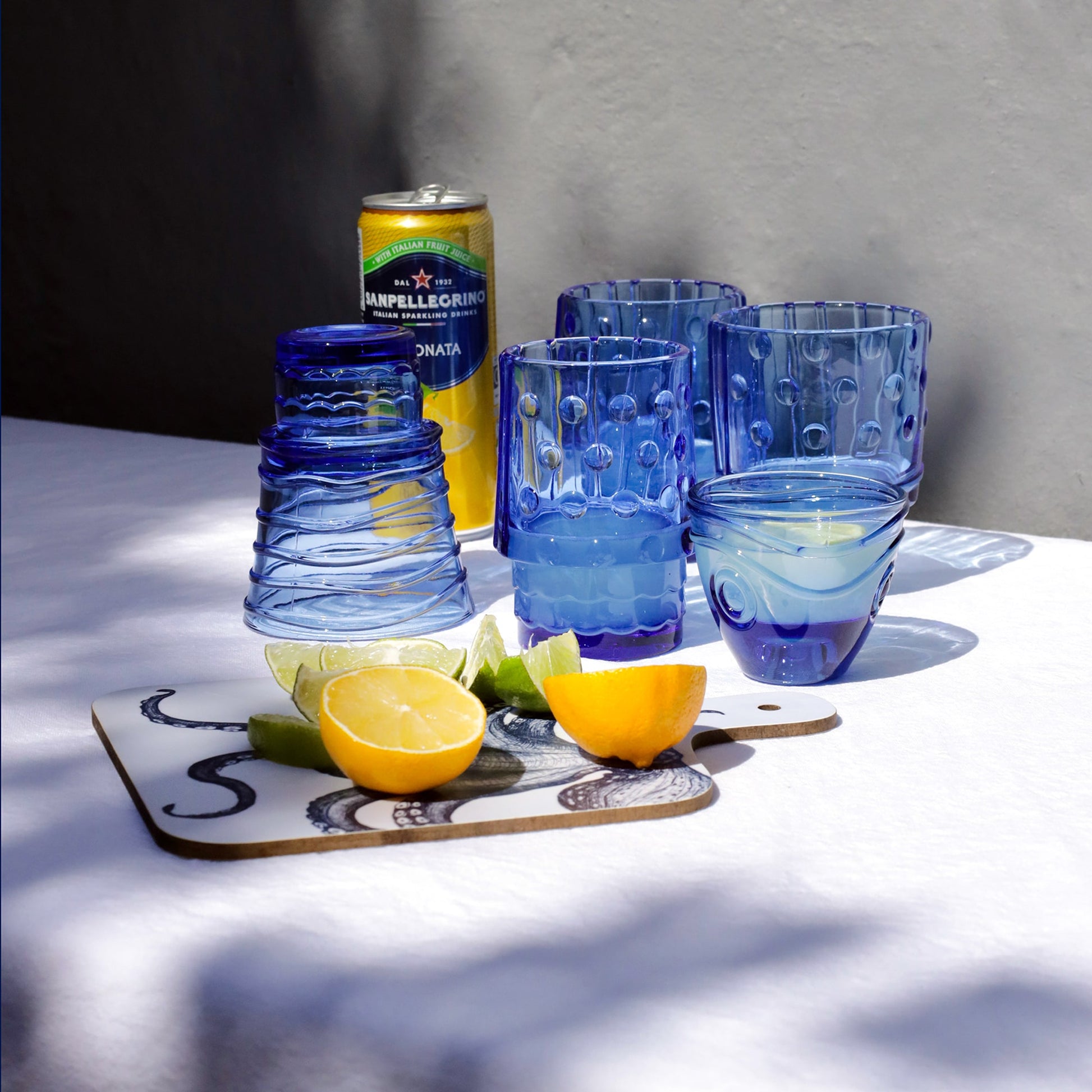 Blue glass tumblers with a can of lemonade on a table with lemon slices and lime.
