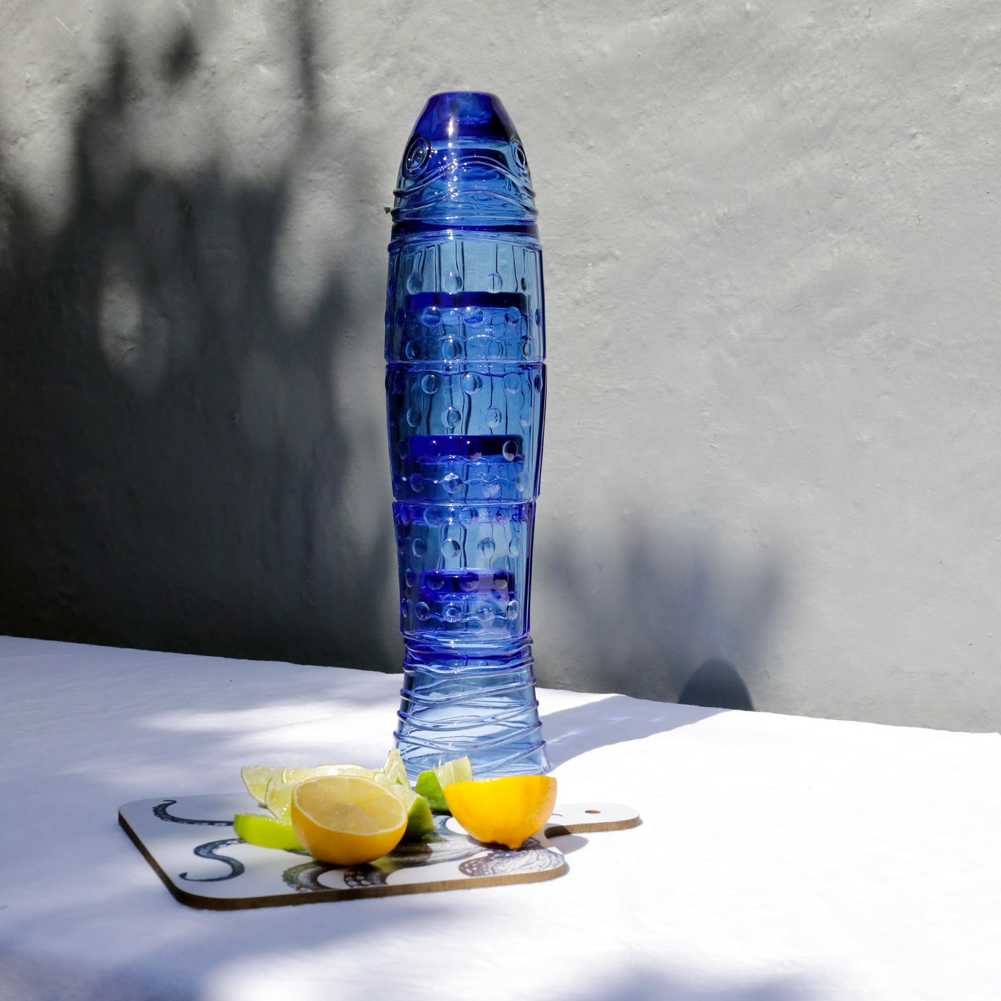 Blue fish stack glasses with a textured design on a white surface with lemons and a chopping board.