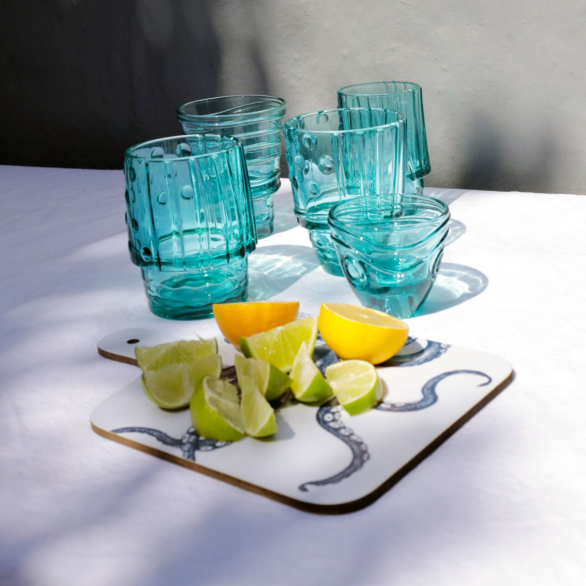 Set of turquoise stacking fish glasses displayed on a white table with a chopping board holding fresh lemon and lime wedges