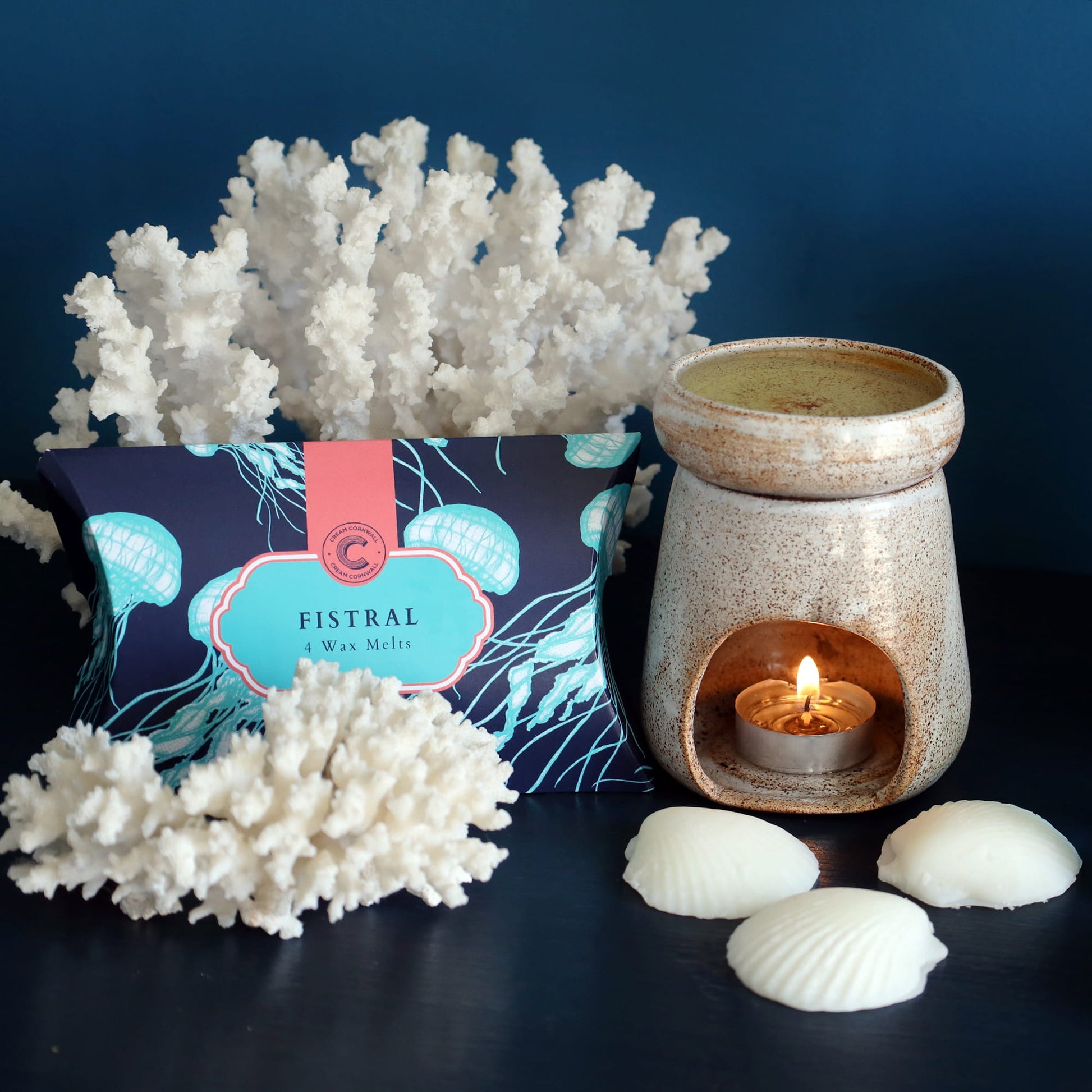  A box of fistral wax melts, decorative coral, and a lit candle holder on a dark surface.