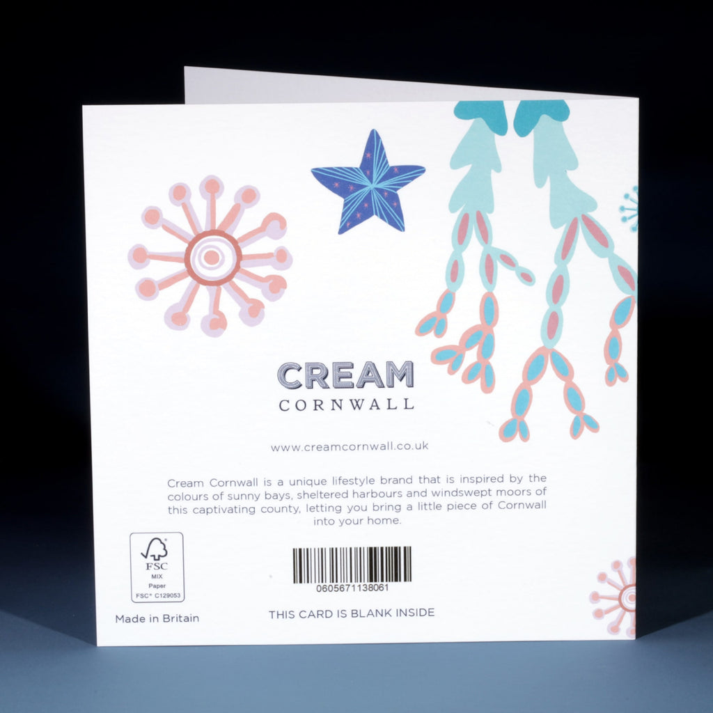 Back of a Cream Cornwall greeting card featuring illustrations of coral, seaweed, and a blue starfish on a white background. Includes the Cream Cornwall logo, a brief brand description, website address, barcode, and note indicating the card is blank inside.