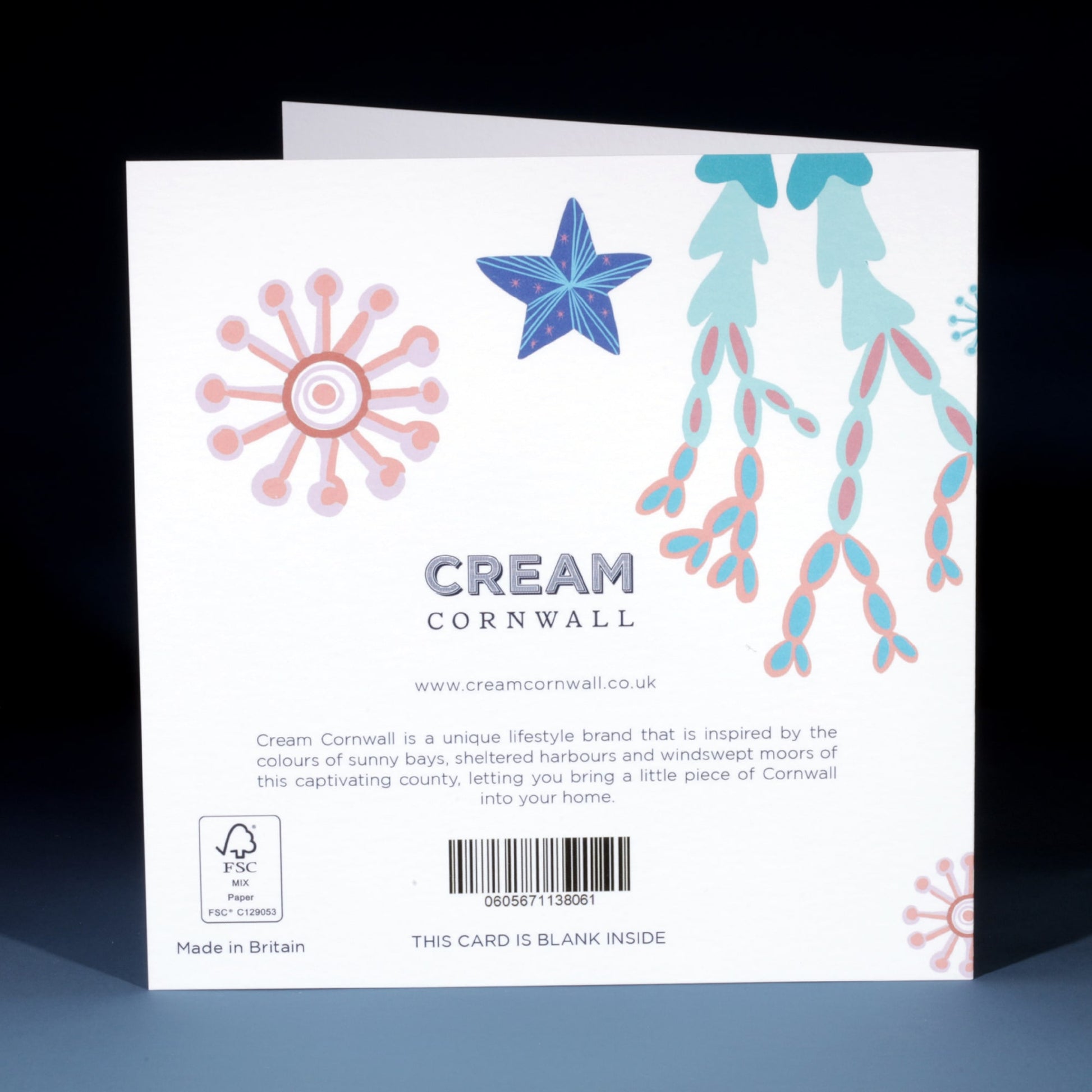 Back of a Cream Cornwall greeting card featuring illustrations of coral, seaweed, and a blue starfish on a white background. Includes the Cream Cornwall logo, a brief brand description, website address, barcode, and note indicating the card is blank inside.