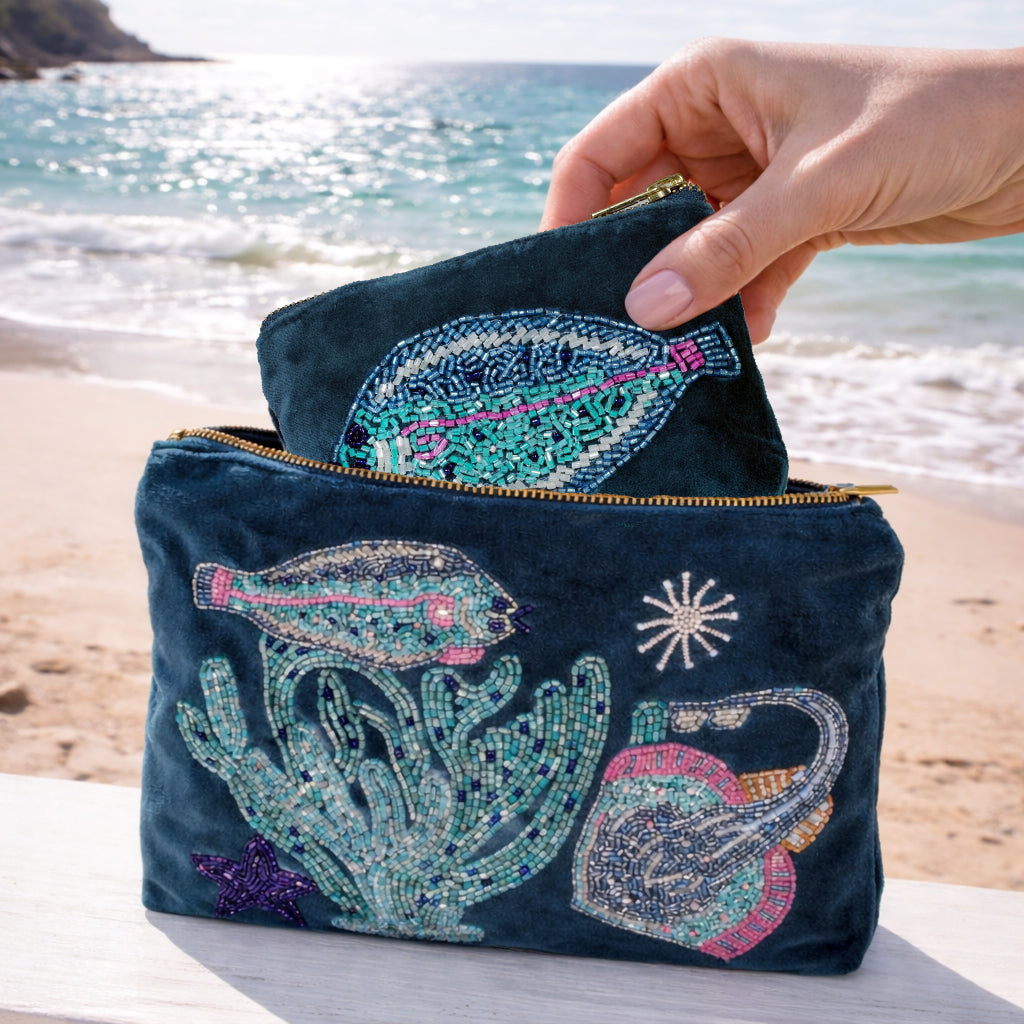 Teal  pouch with beaded sea-themed designs held by a hand on a beach.