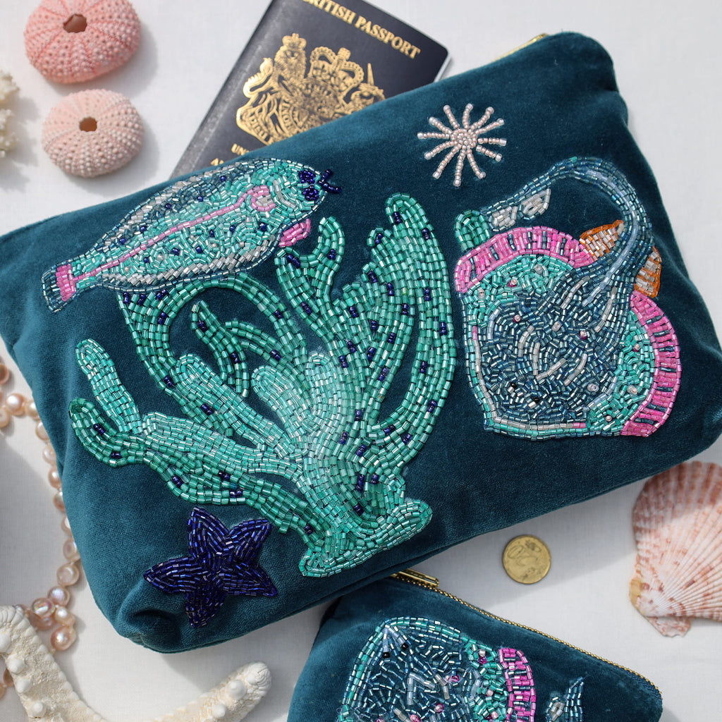 Beaded clutch with ocean-themed design on a white surface with shells and a passport.