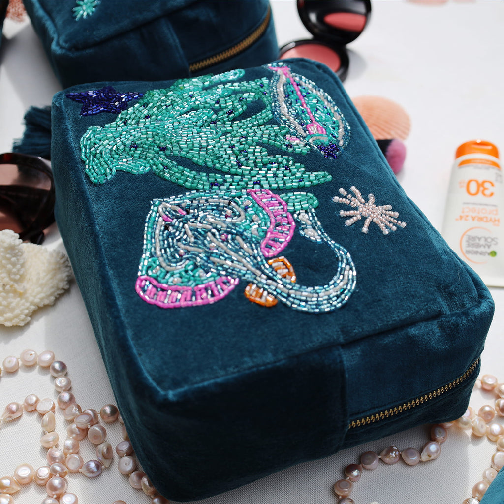Blue pouch with embroidered sea creature design on a white surface with jewelry and makeup items.