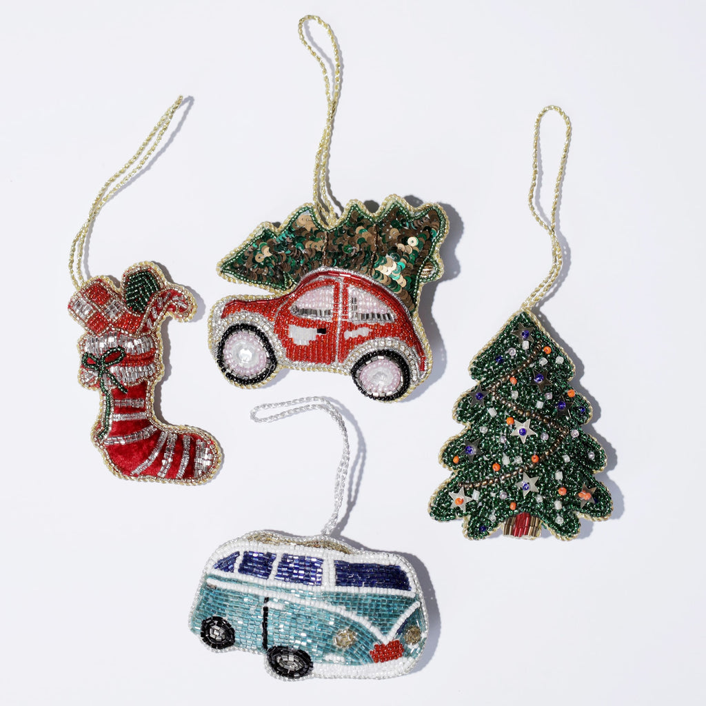 Flat lay of five festive beaded ornaments on a white background, including a red stocking with green and white accents, a red car carrying a green Christmas tree on top, a decorated Christmas tree, a turquoise and white retro van, and a green pine tree. Each ornament is detailed with colorful beads and sequins, giving a vibrant holiday charm to the collection.