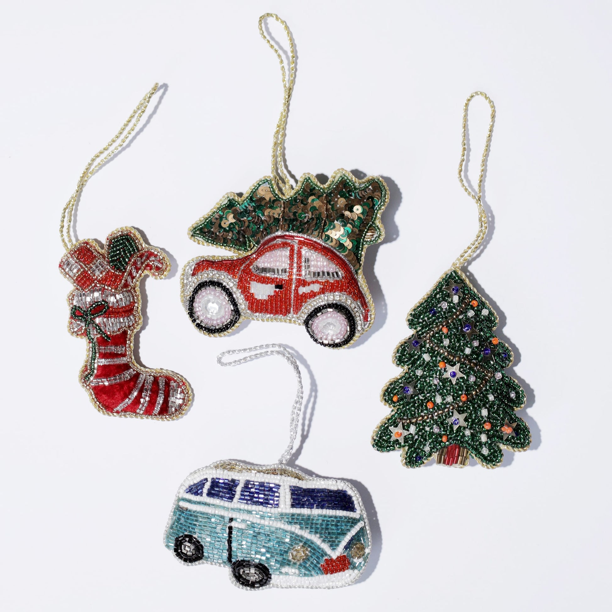 Flat lay of five festive beaded ornaments on a white background, including a red stocking with green and white accents, a red car carrying a green Christmas tree on top, a decorated Christmas tree, a turquoise and white retro van, and a green pine tree. Each ornament is detailed with colorful beads and sequins, giving a vibrant holiday charm to the collection.