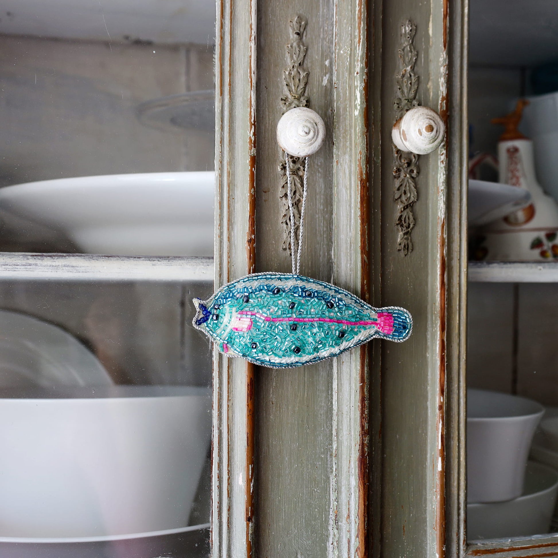 Decorative fish ornament hanging on a vintage cabinet with dishes in the background