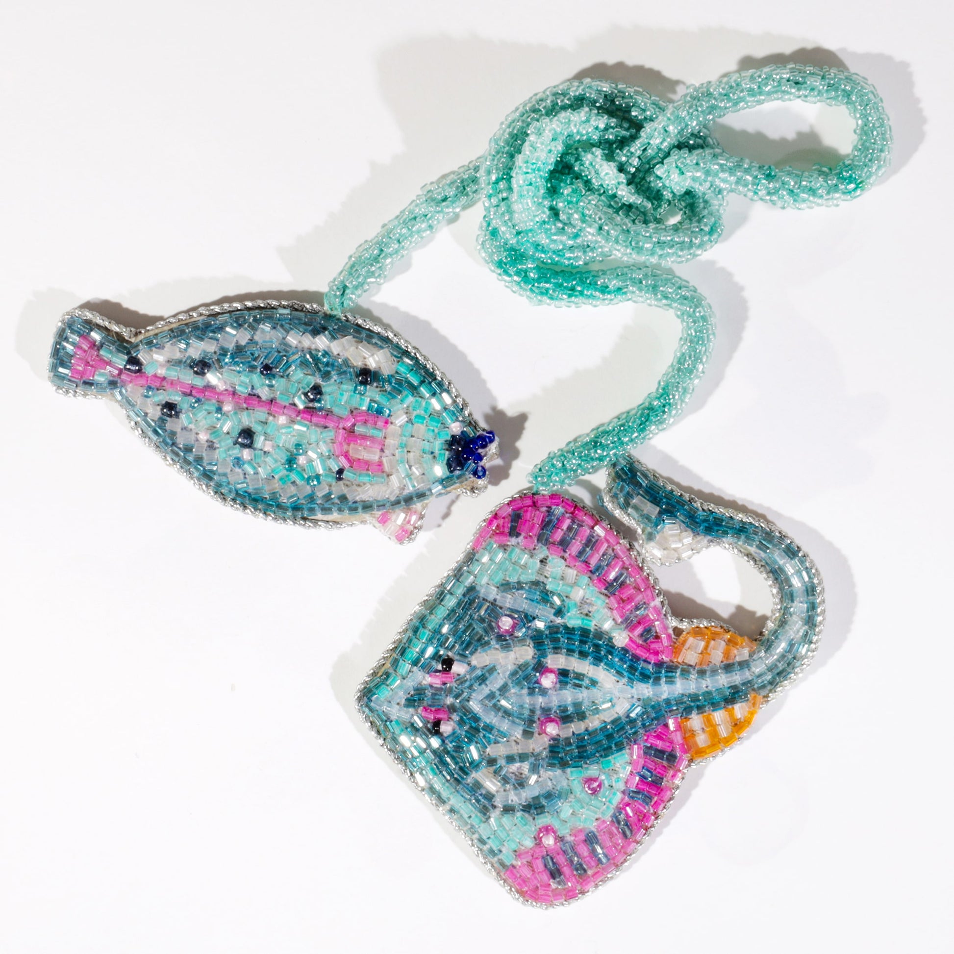 Two beaded ocean-themed bag charms, one shaped like a turquoise fish and the other like a stingray, with pink, blue, and silver detailing on a pale background.