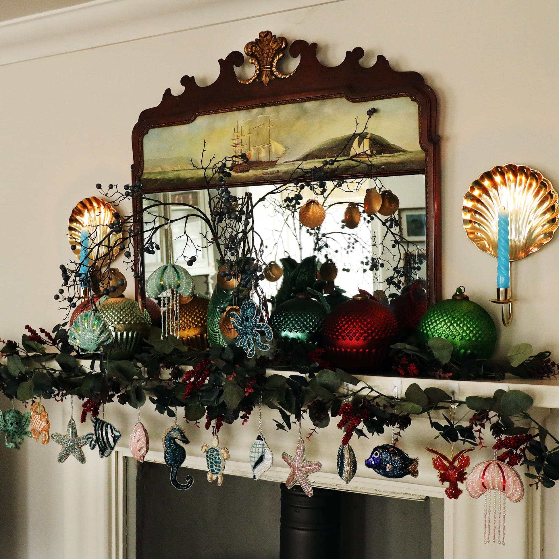 Lots of beaded coastal decorations hanging from a mantlepiece adorned with winter foliage and oversized vintage glass baubles.