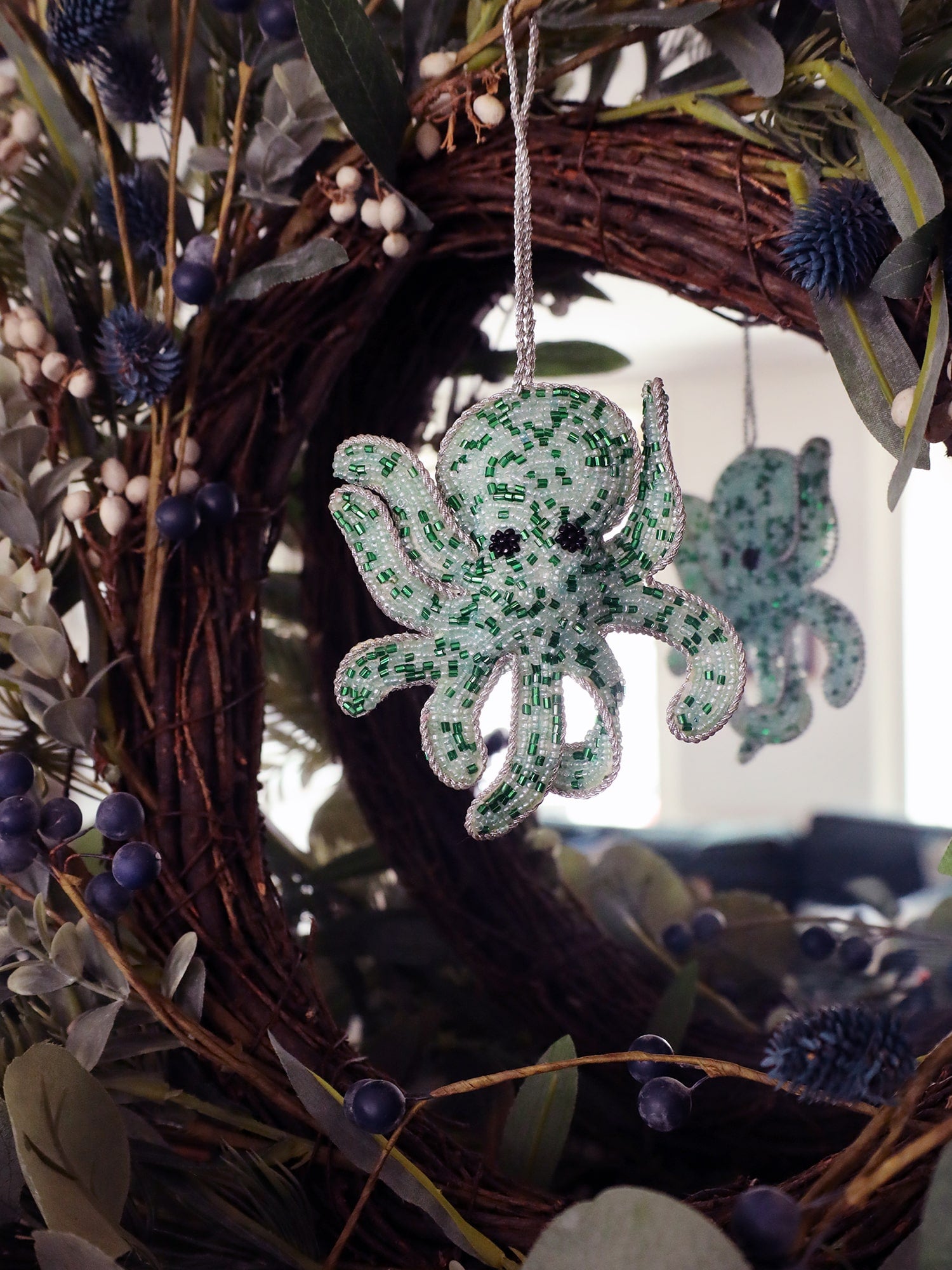 Beaded aqua coloured octopus hanging decoration reflected in a mirror with winter foliage around it