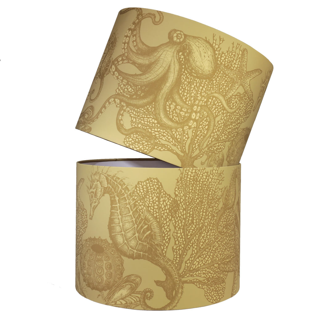 Two gold lampshades featuring an intricate under-the-sea design with illustrations of seahorses, octopuses, coral, and seashells in a metallic finish, stacked at an angle against a white background.