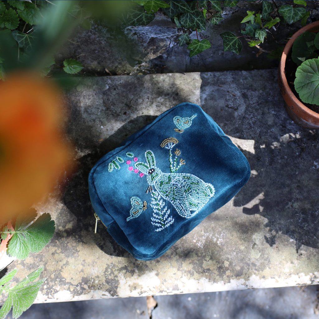 Blue embroidered pouch with a rabbit design on a stone surface with plants around