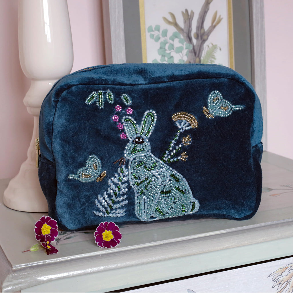 Teal  embroidered pouch with a hare design on a white surface.