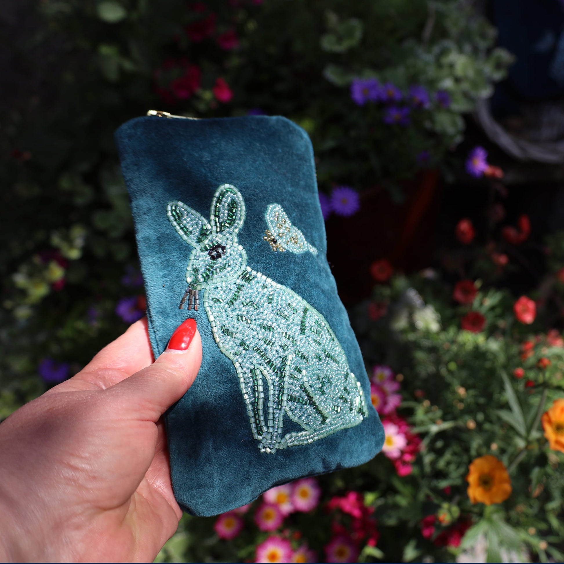 Blue embroidered pouch with a rabbit design held by a hand against a floral background