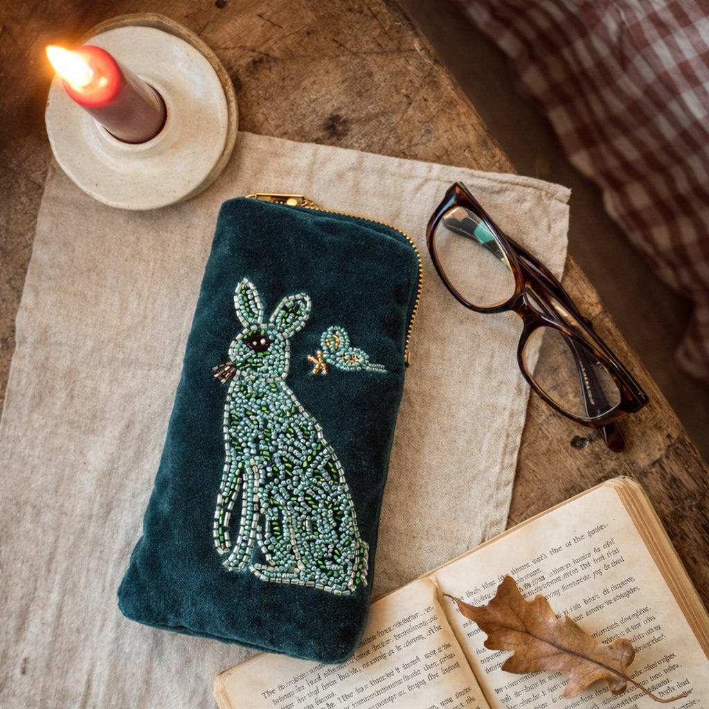 Teal  beaded pouch with hare design on a wooden surface with glasses and book.