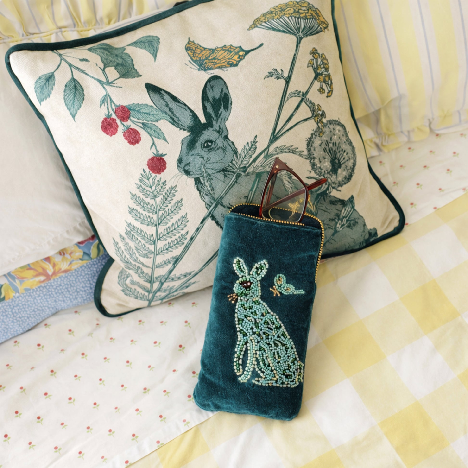 Decorative pillow with hare and floral design on a bed with a matching pouch.