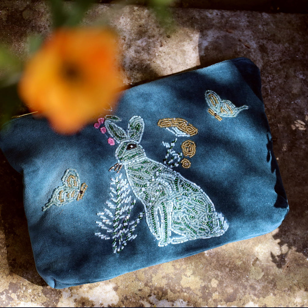 Embroidered blue pouch with a rabbit design on a textured surface with an orange flower.