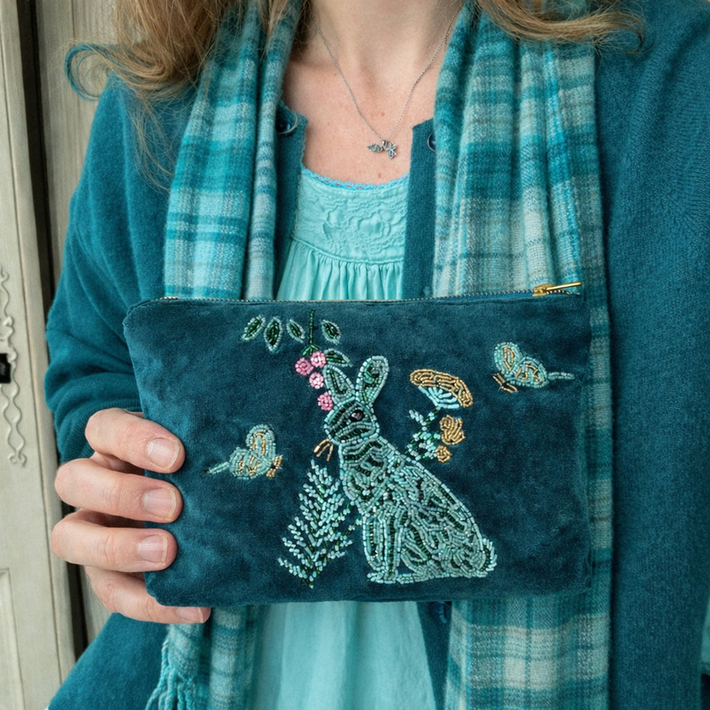 Person holding a blue embroidered pouch with a hare design, wearing a matching outfit.
