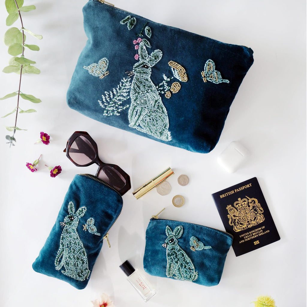 Teal beaded pouches with floral designs on a white surface with accessories.