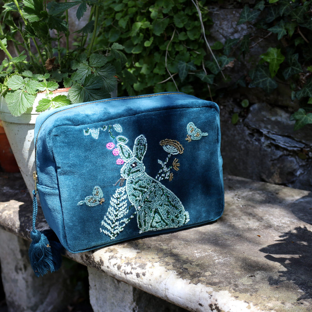 Blue embroidered bag with a rabbit design on a stone surface with greenery in the background