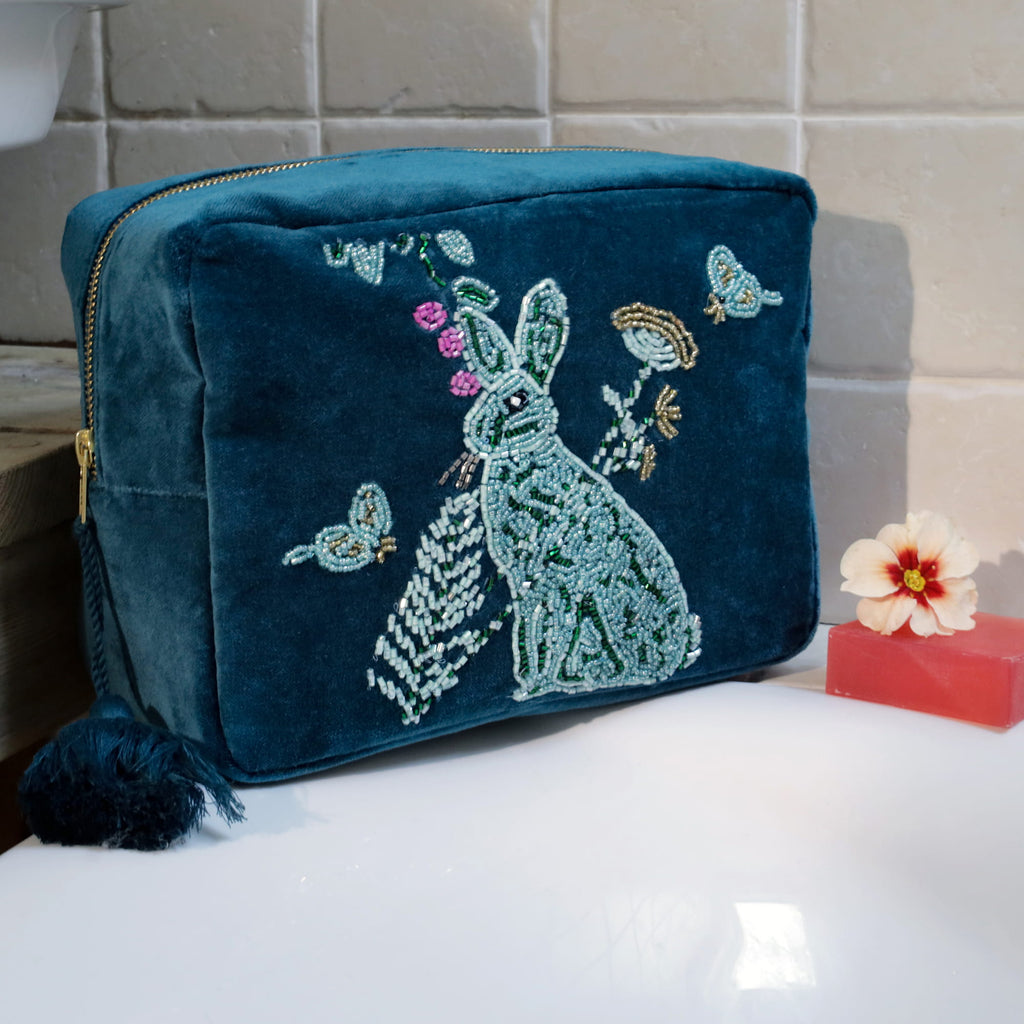 Teal beaded pouch with a rabbit design on a bathroom counter.