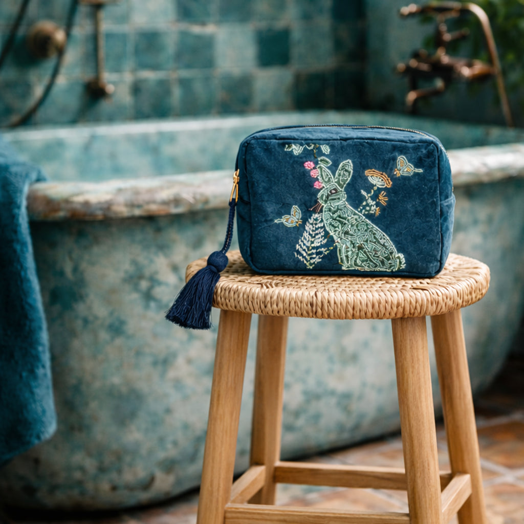 Beaded teal pouch with a rabbit design on a wooden stool in front of a vintage bathtub.