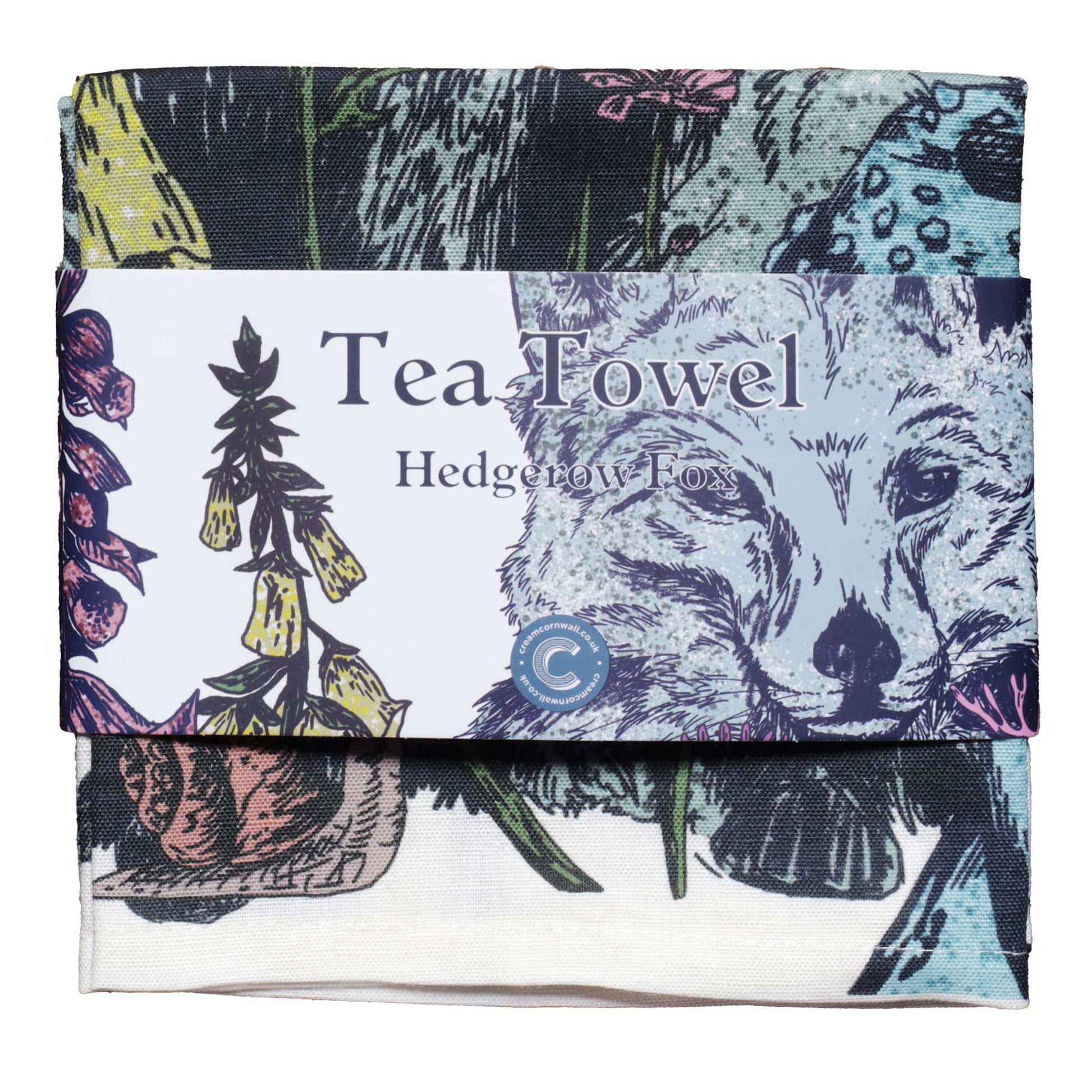 Folded tea towel with a woodland-themed print featuring a fox surrounded by wildflowers, foxgloves, and mushrooms. The towel is wrapped with a branded label that reads 'Tea Towel – Hedgerow Fox,' showcasing part of the detailed nature-inspired illustration in shades of green, yellow, pink, and blue.