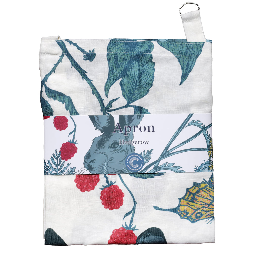 Folded apron with a nature-inspired print featuring a hare, wildflowers, raspberry vines, and a butterfly. The apron is wrapped with a branded label that reads 'Apron – Hedgerow,' highlighting the rustic countryside design in shades of green, red, and yellow on a white background