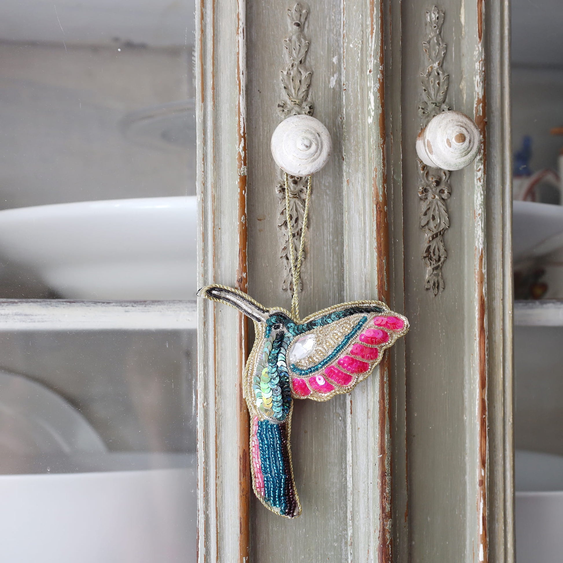 Decorative hummingbird ornament hanging on a vintage-style door with ornate handles.