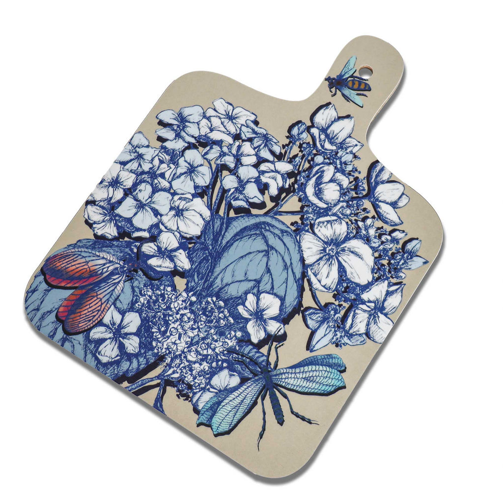 Cream Cornwall hydrangea chopping board featuring intricate blue and white botanical illustrations, colourful dragonflies and a bee on a soft cream background, with rounded corners and a handle with a hanging hole.