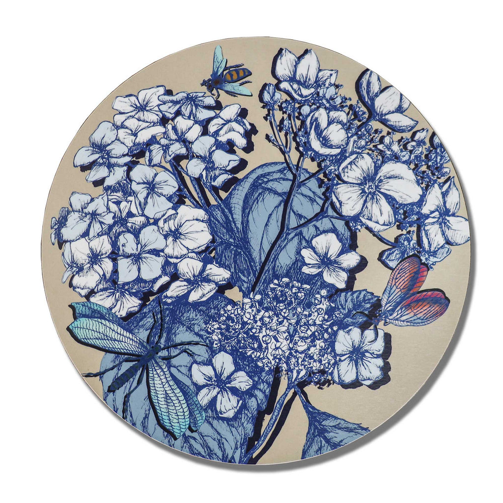
Round decorative placemat featuring intricate blue botanical illustrations of blooming hydrangeas, delicate flowers and large leaves on a soft beige background. The design includes a turquoise dragonfly, a blue and yellow bee, and a butterfly with coral-pink wings, creating an elegant, nature-inspired pattern. Photographed from above against a plain white background.