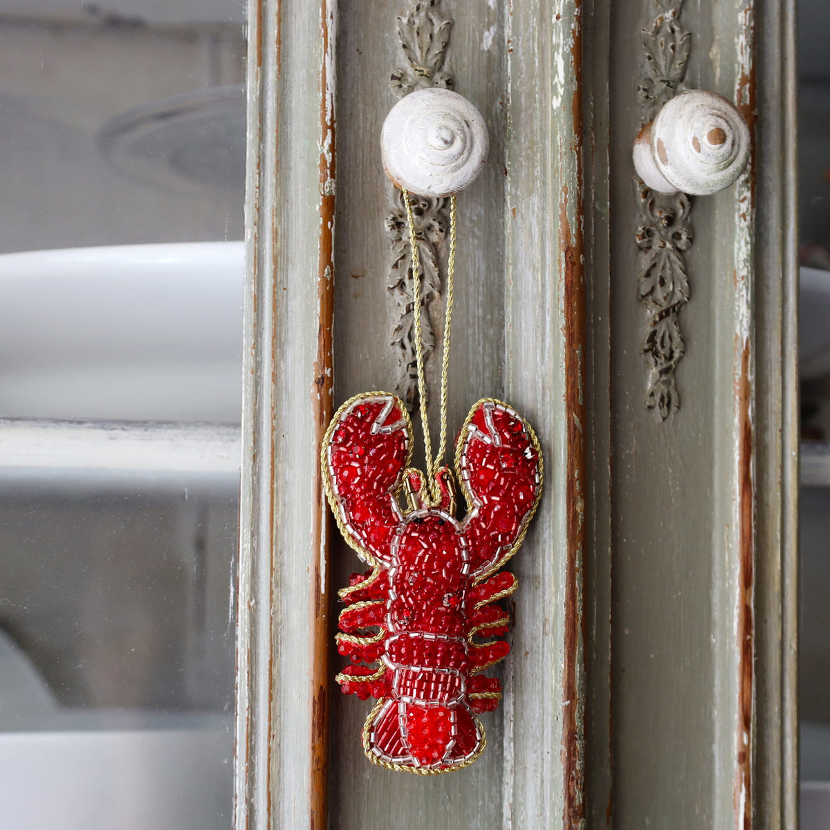 Decorative red lobster ornament hanging on a rustic wooden door with metal knobs.