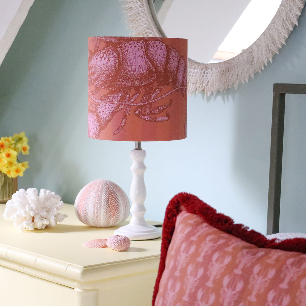 Decorative lamp with pink shade on a table next to a mirror and decorative items.