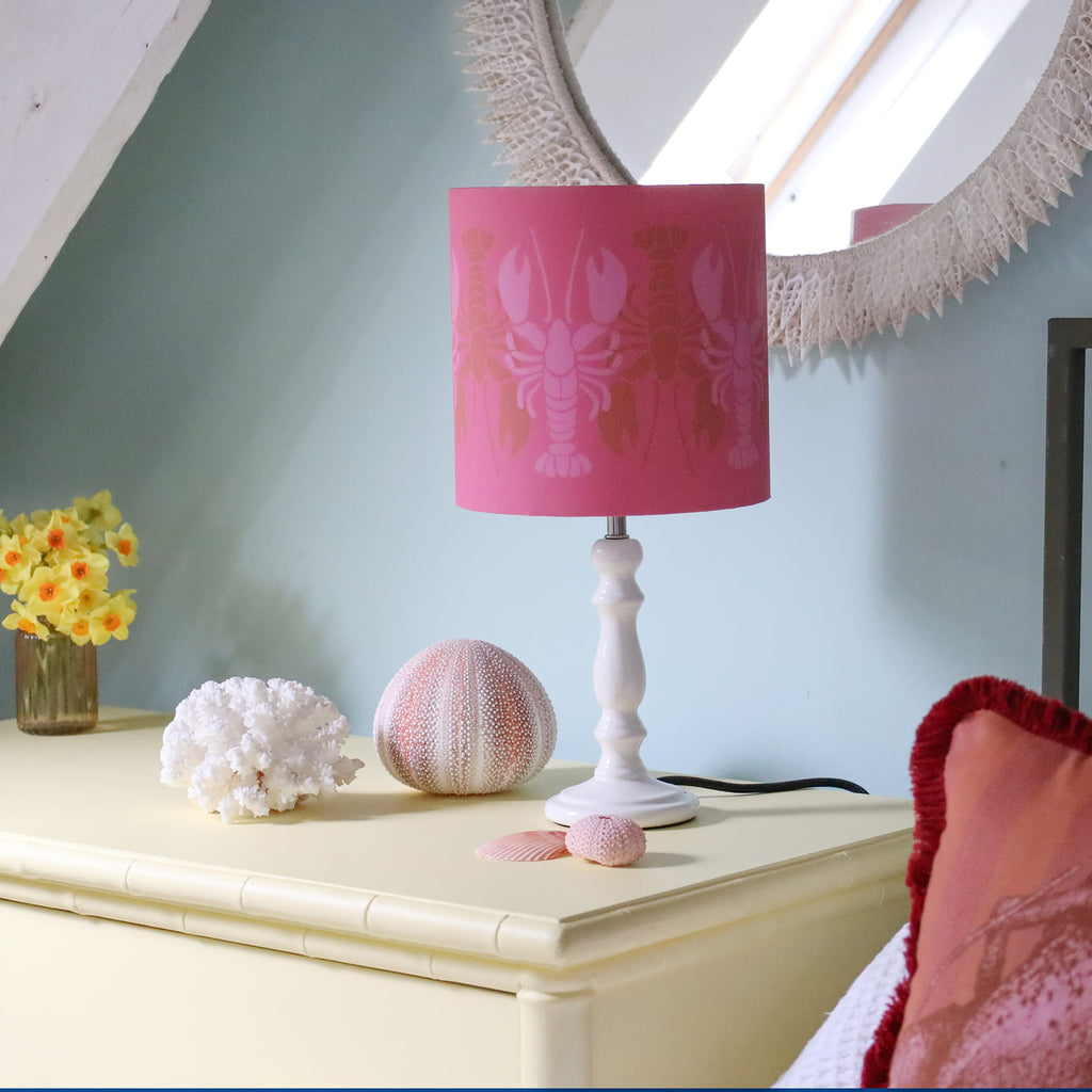 Pink lamp with lobster design on a white table next to decorative items.