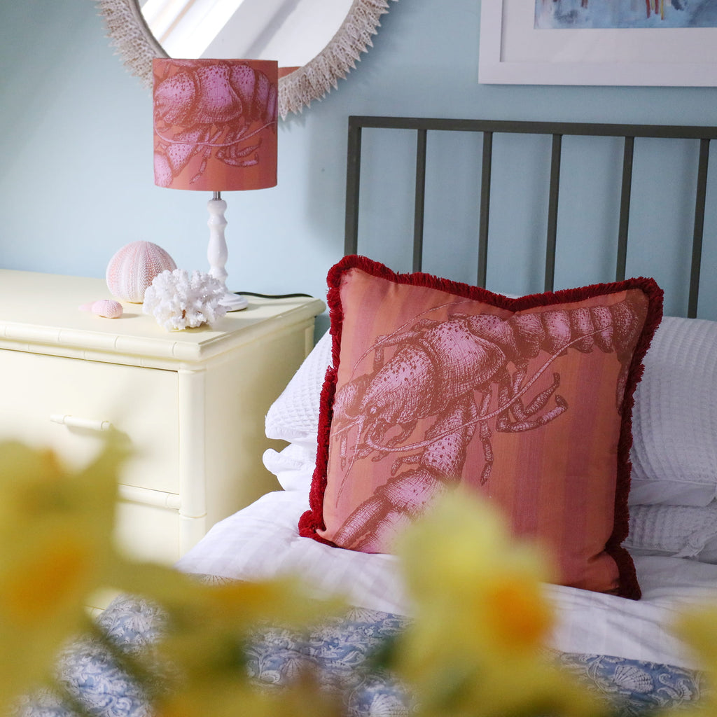 Decorative pillow on a bed with a lamp and nightstand in the background