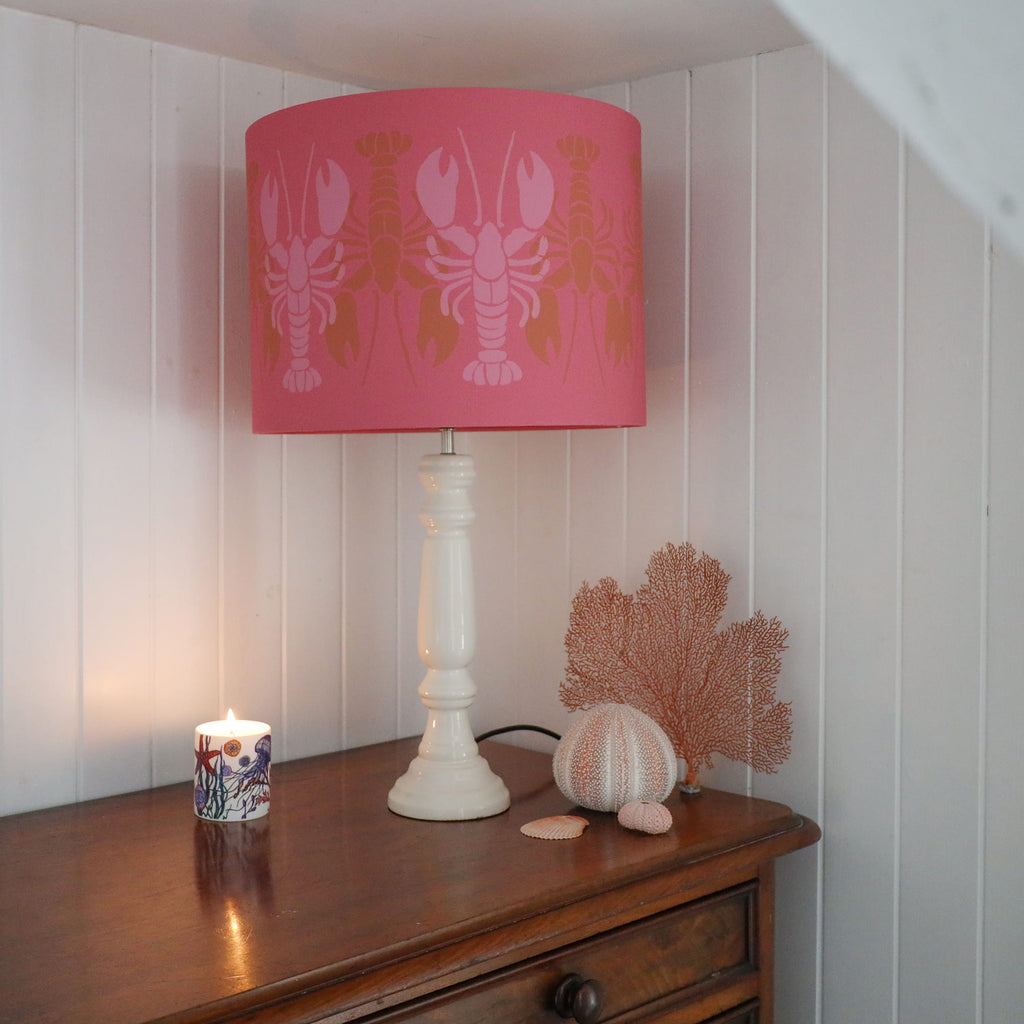 Lamp with pink lampshade featuring lobster design on a wooden surface.