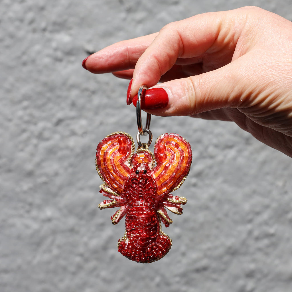 Red lobster keychain held by a hand with red nail polish against a gray background