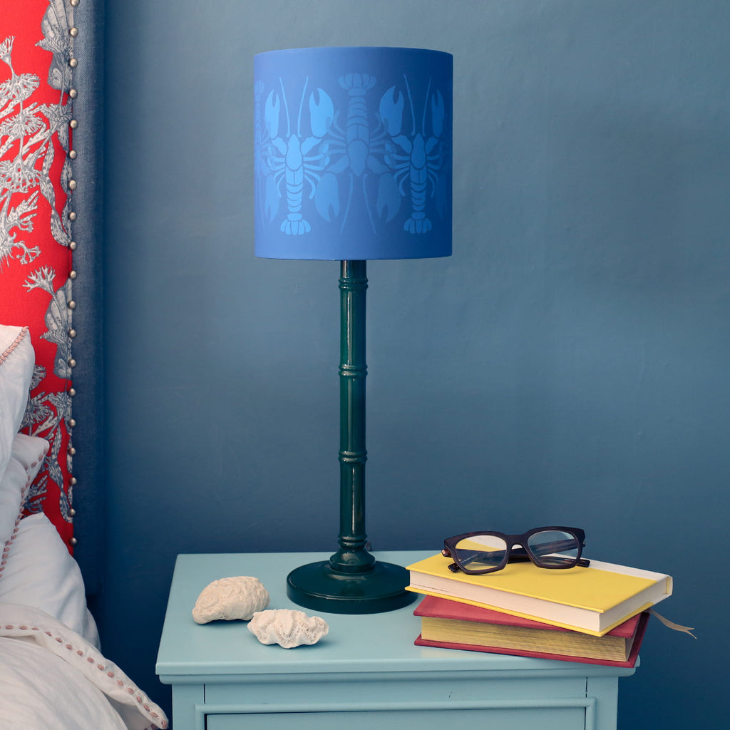Blue lamp with lobster design on a bedside table against a blue wall.