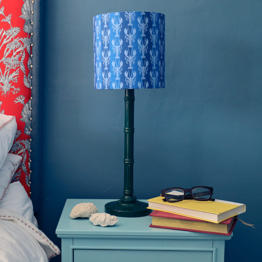 Table lamp with blue patterned shade on a nightstand next to a bed with red floral headboard.