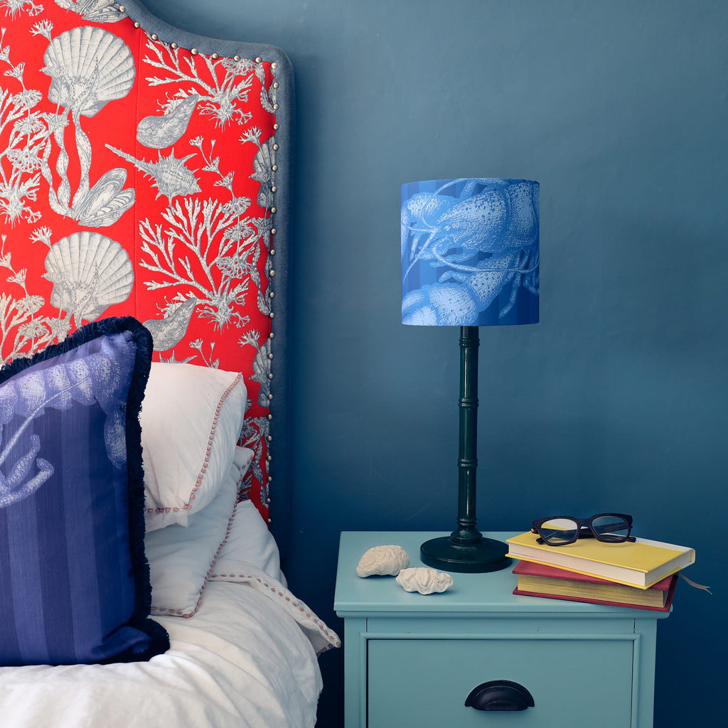 Bedroom with red floral headboard, blue lamp, and teal nightstand with books and sunglasses.