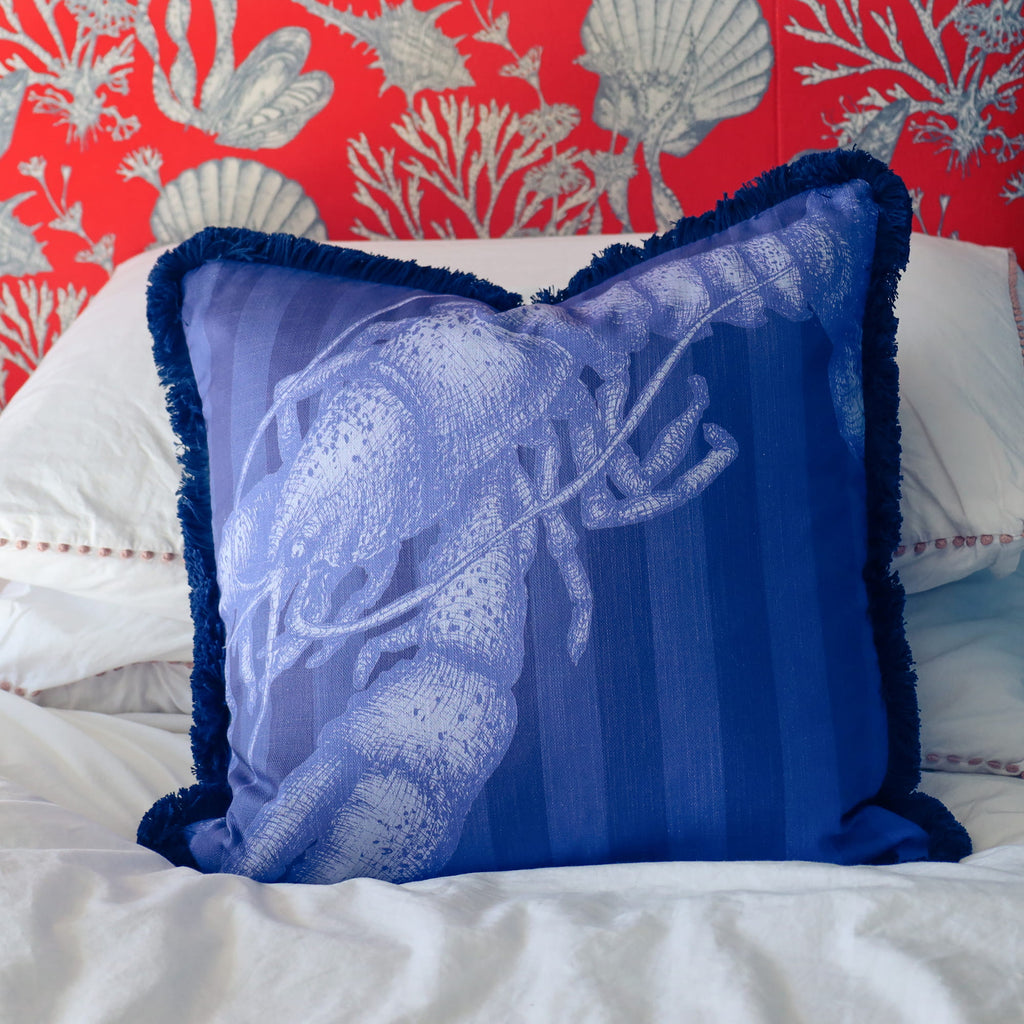 Blue decorative pillow with white patterns on a bed with a red and gray coral wallpaper.