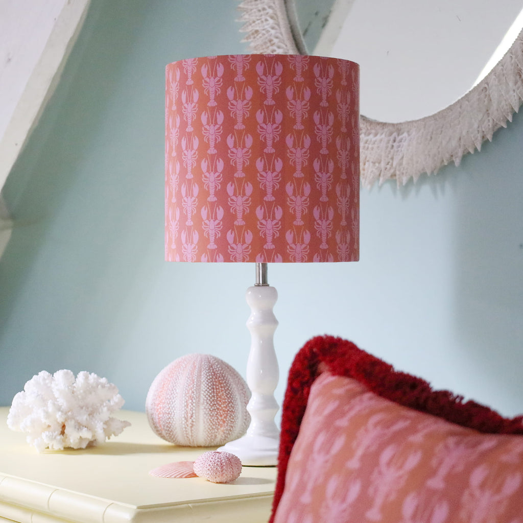Lamp with a pink mini lobster patterned shade on a table with decorative items.