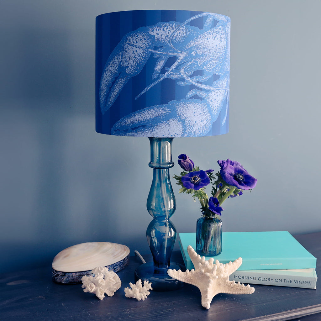 Blue lamp with floral design, books, and decorative items on a table against a blue wall.