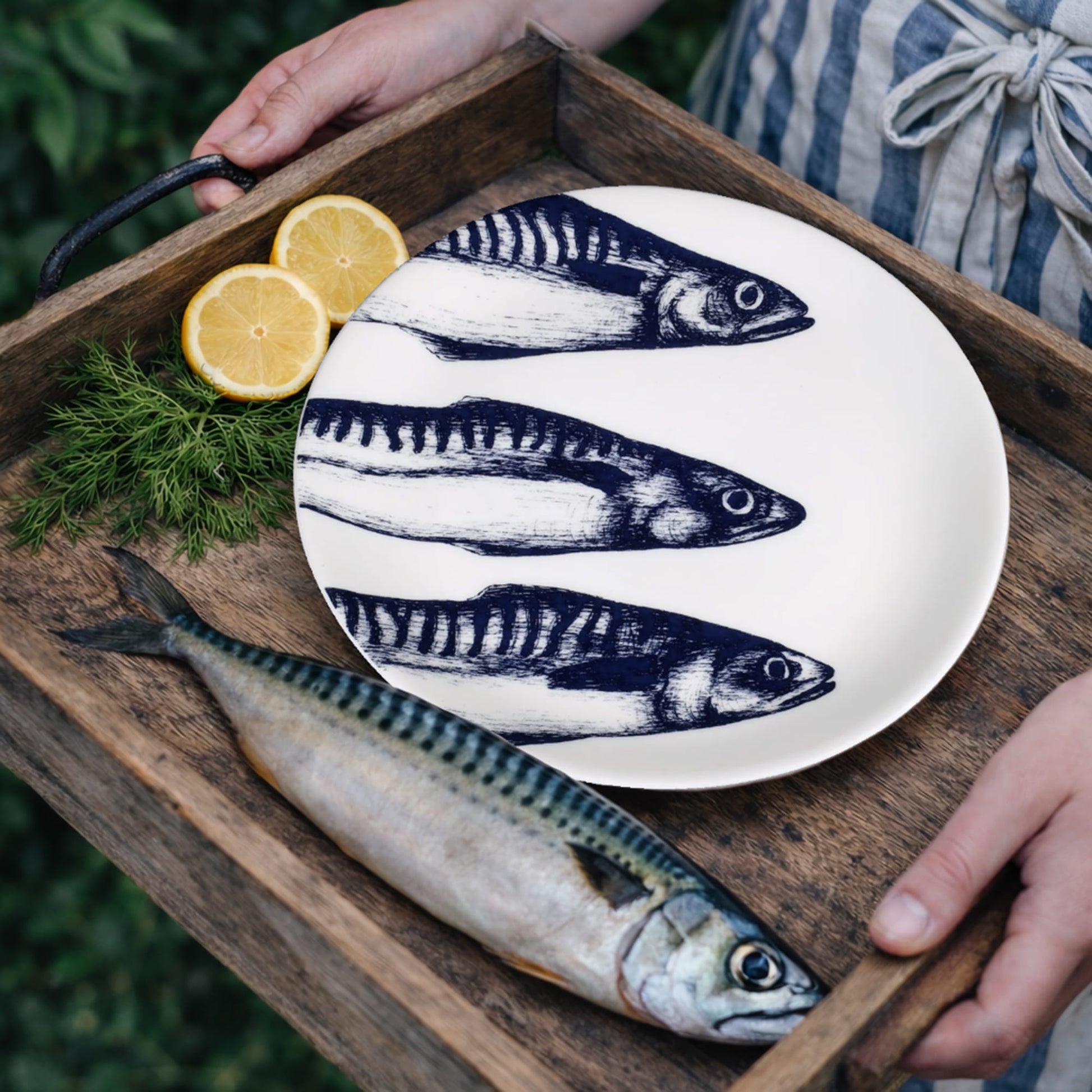 White plate with fish design on a wooden tray with a fresh fish and lemon.