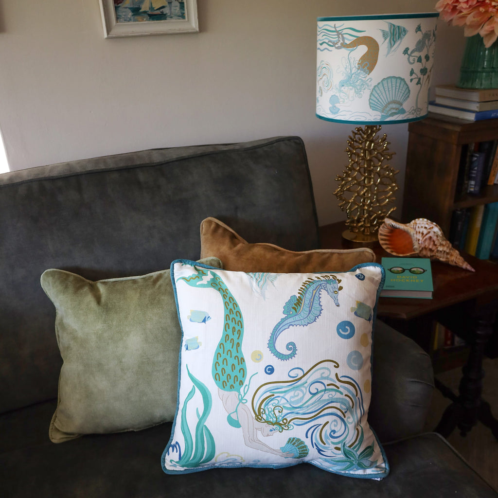 Cream Cornwall Mermaid cushion styled on a charcoal armchair with velvet cushions, alongside a coordinating coastal table lamp for a relaxed seaside-inspired interior.