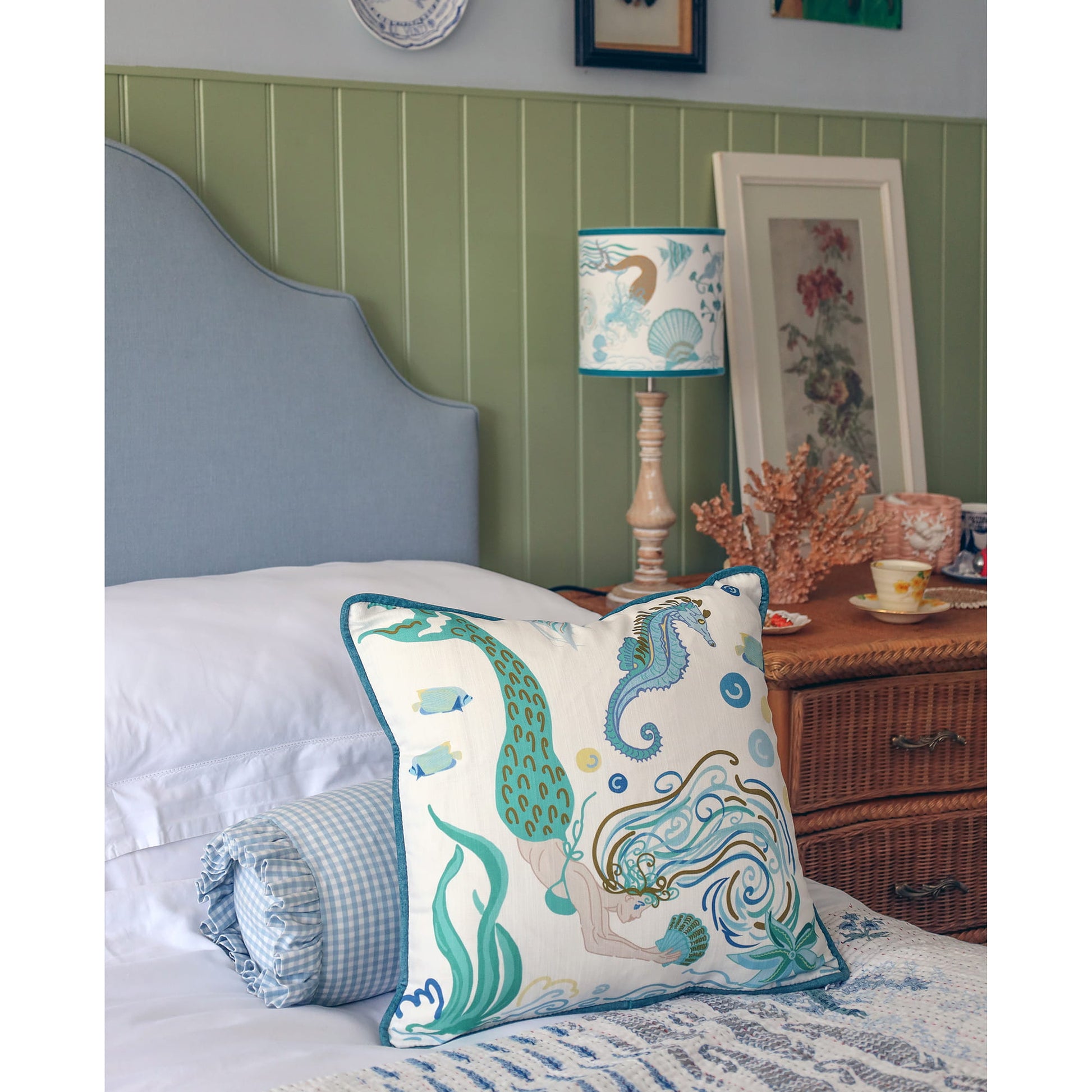 Cream Cornwall Mermaid cushion styled on a bed with blue gingham bedding and a coordinating Mermaid lampshade, creating a calm coastal bedroom inspired by the Cornish coast.