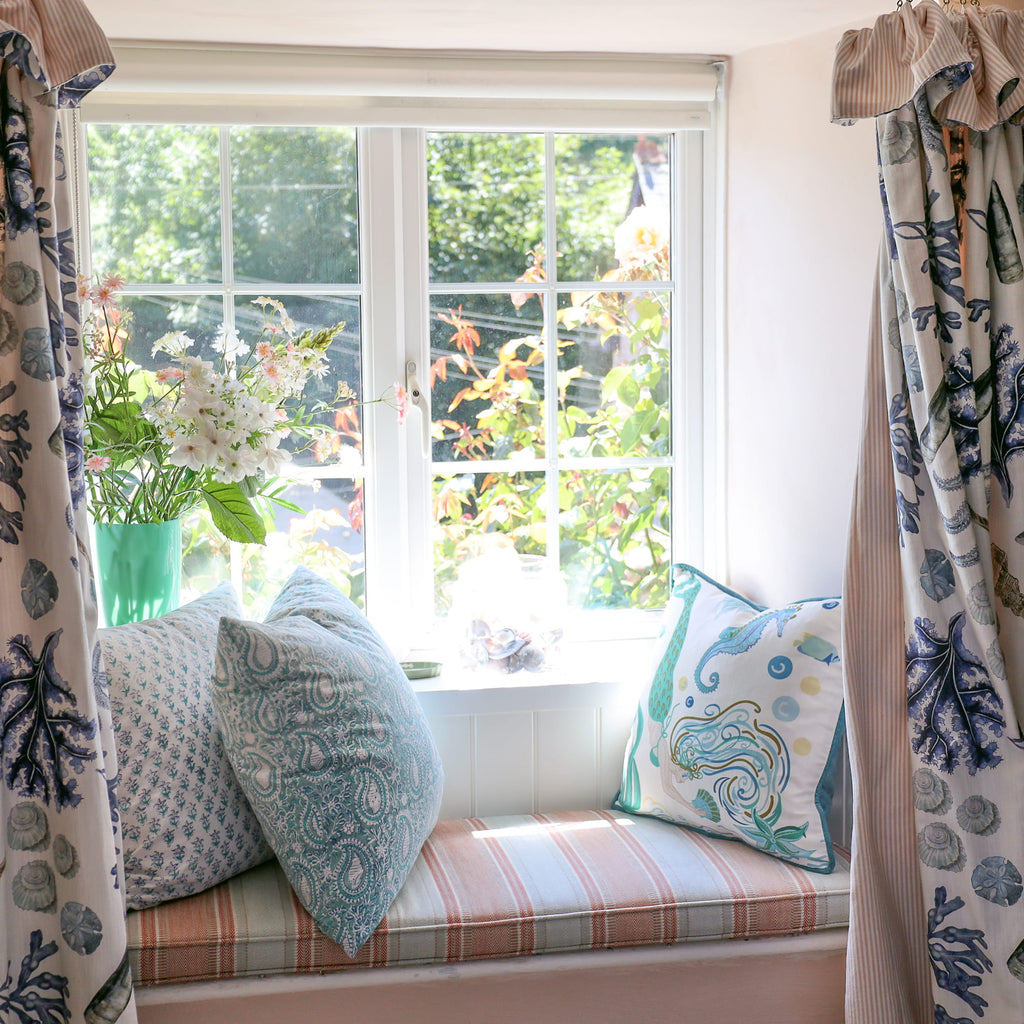 Cream Cornwall Mermaid cushion styled on a window seat with blue patterned cushions and coordinating coastal curtains, creating a light and relaxed seaside-inspired home.