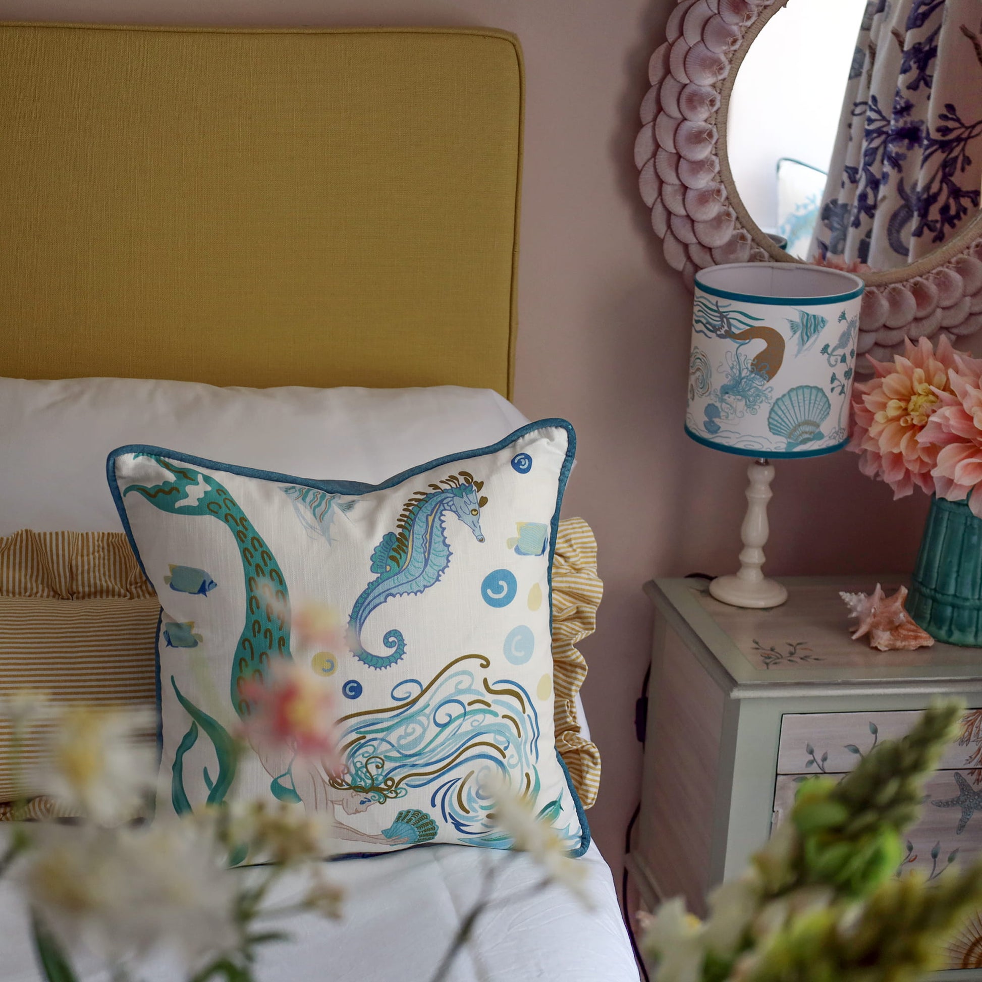Cream Cornwall Mermaid cushion styled on a bed with striped bedding and a coordinating Mermaid lampshade, creating a bright and inviting coastal-inspired bedroom.
