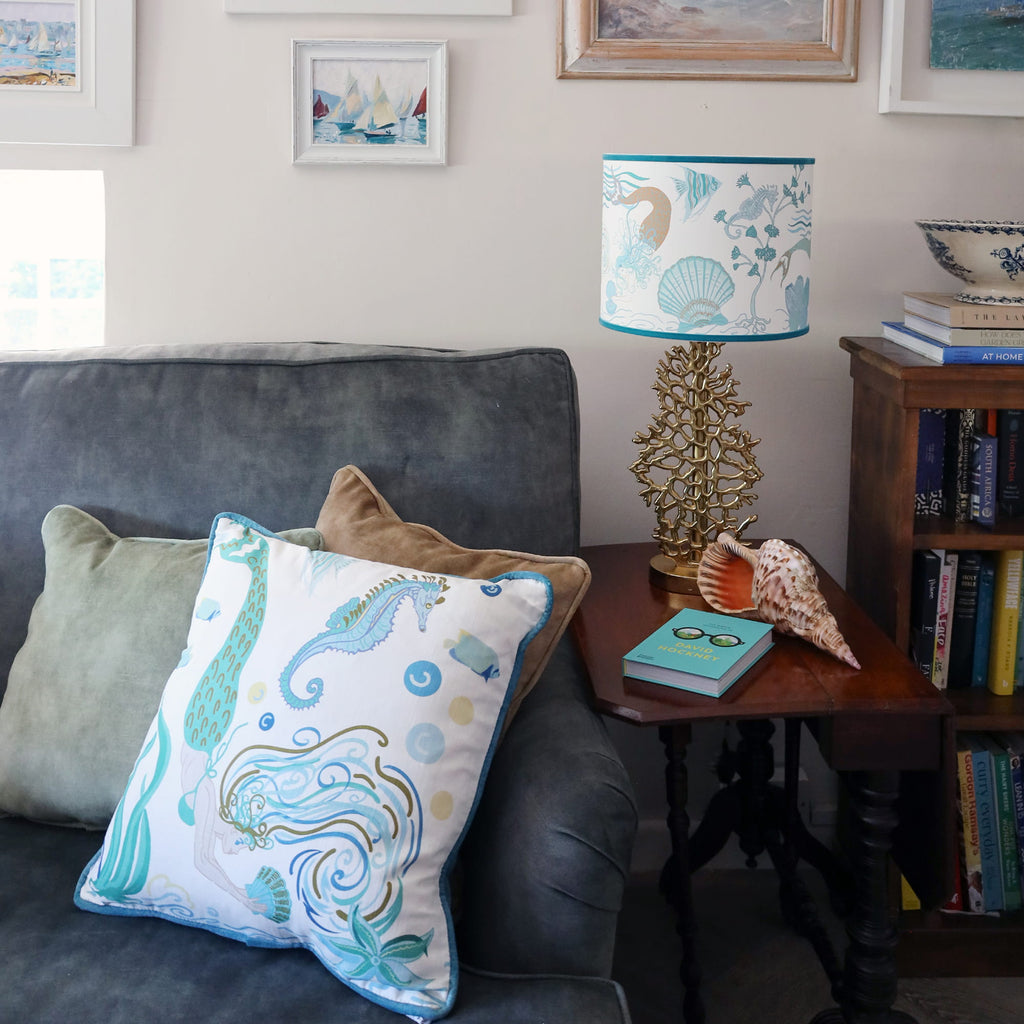 Cream Cornwall Mermaid cushion styled on a charcoal sofa with soft velvet cushions, alongside a coordinating Mermaid lampshade and coastal accessories in a relaxed seaside-inspired living room.